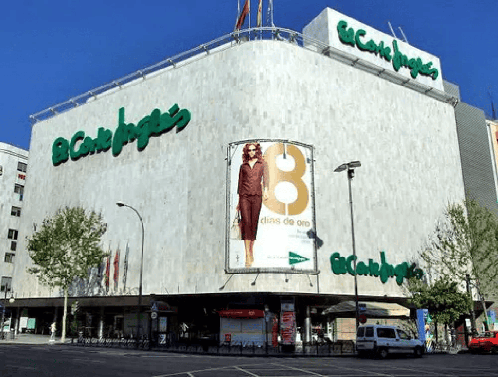 External image of El Corte Ingles department store in downtown Madrid. A green scripted logo stands out against the grey color of the building.